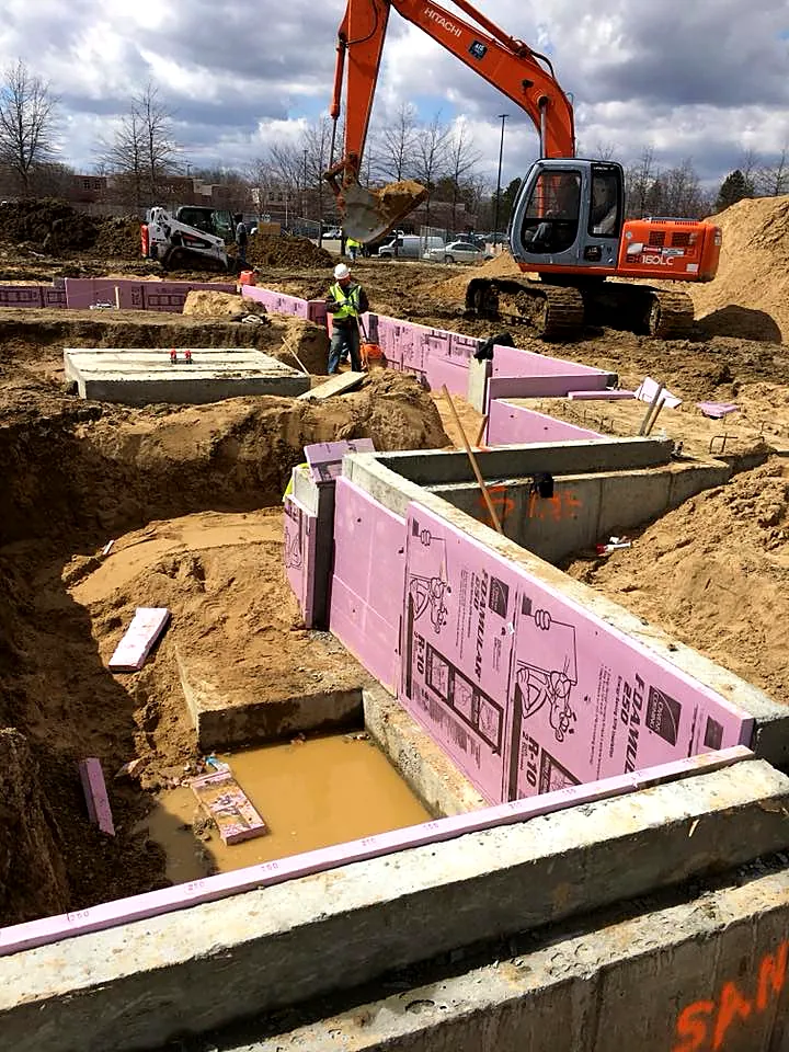Insulated foundation walls being formed in an excavation with an excavator on site