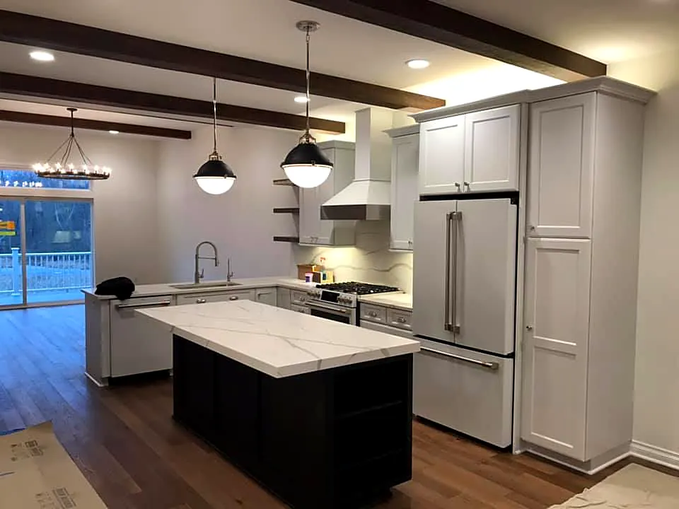 New kitchen with white shaker cabinets, a dark island, wood ceiling beams and black pendant lights