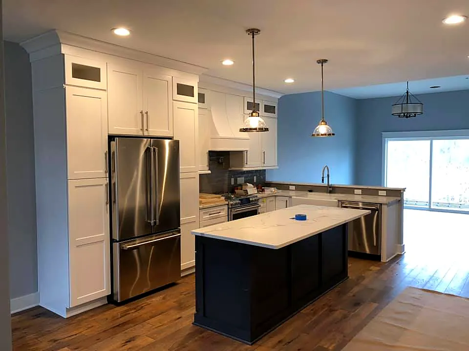 Remodeled kitchen with white cabinets, a dark island, quartz countertops and pendant lights