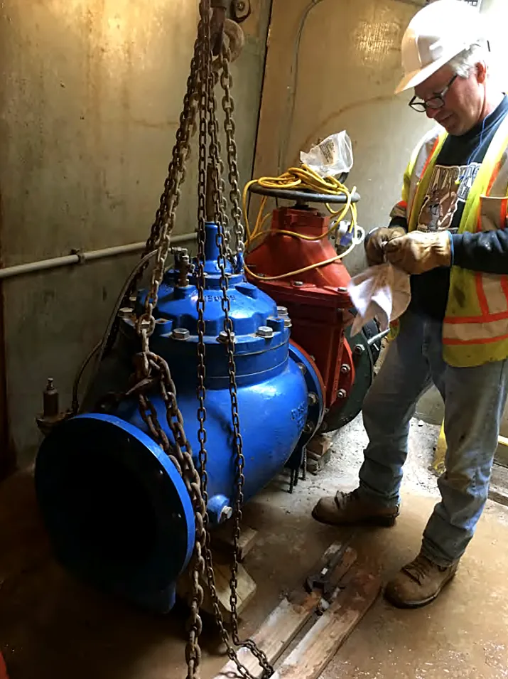 Worker rigging and installing a large blue water valve