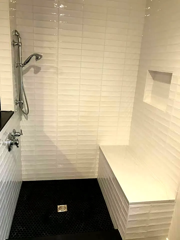 Walk-in shower with white subway tile, built-in bench and black hex tile floor